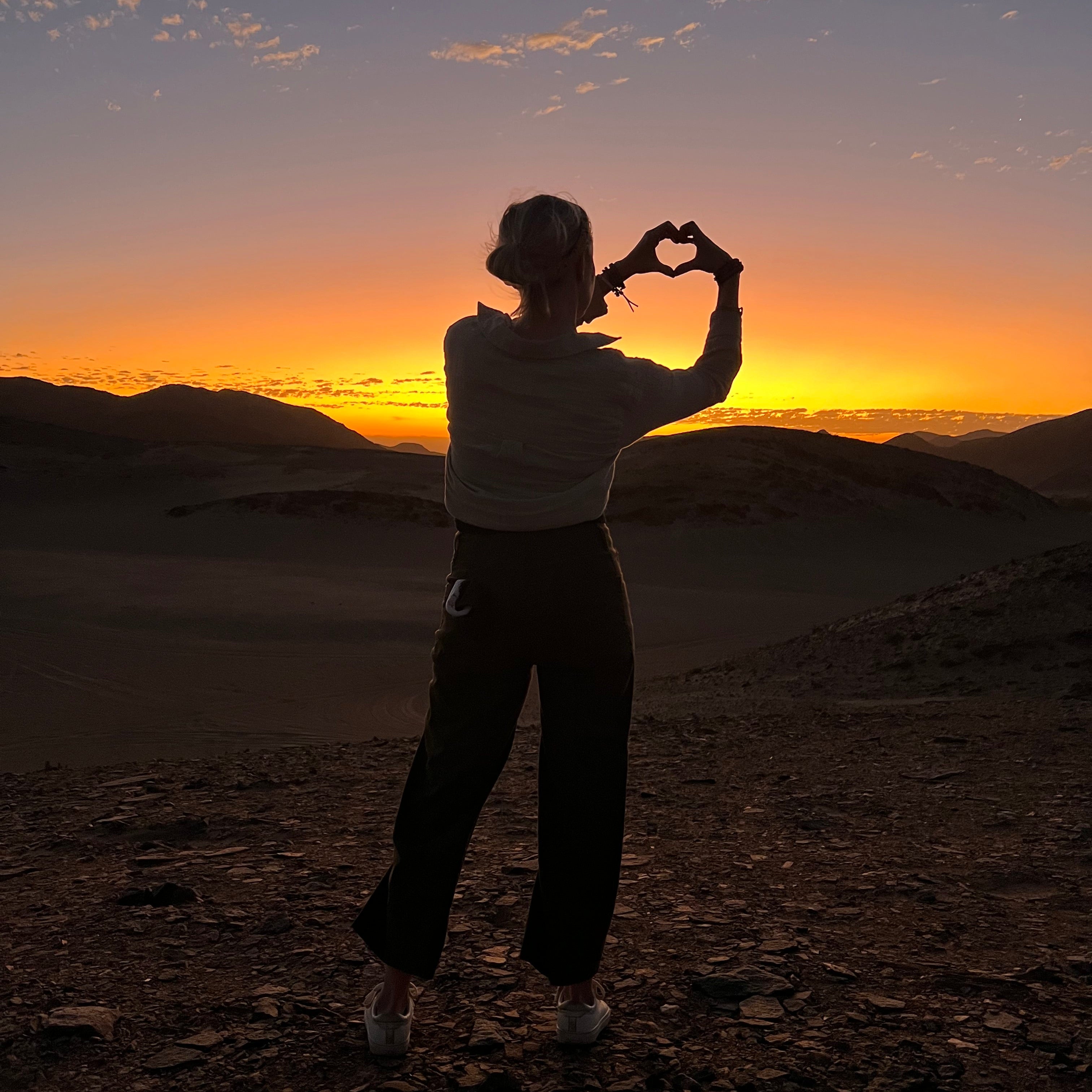 Petite Protea founder in Namibia at sunset making a heart with her hands, ethical online jewelry