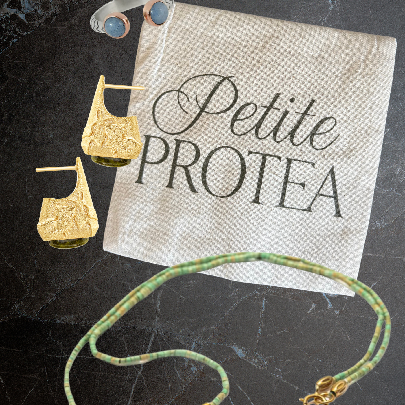 Silver Aquamarine ring, Handmade gold and jasper earrings, ethical turquoise and gold plated necklace in front of a Petite Protea jewelry bag