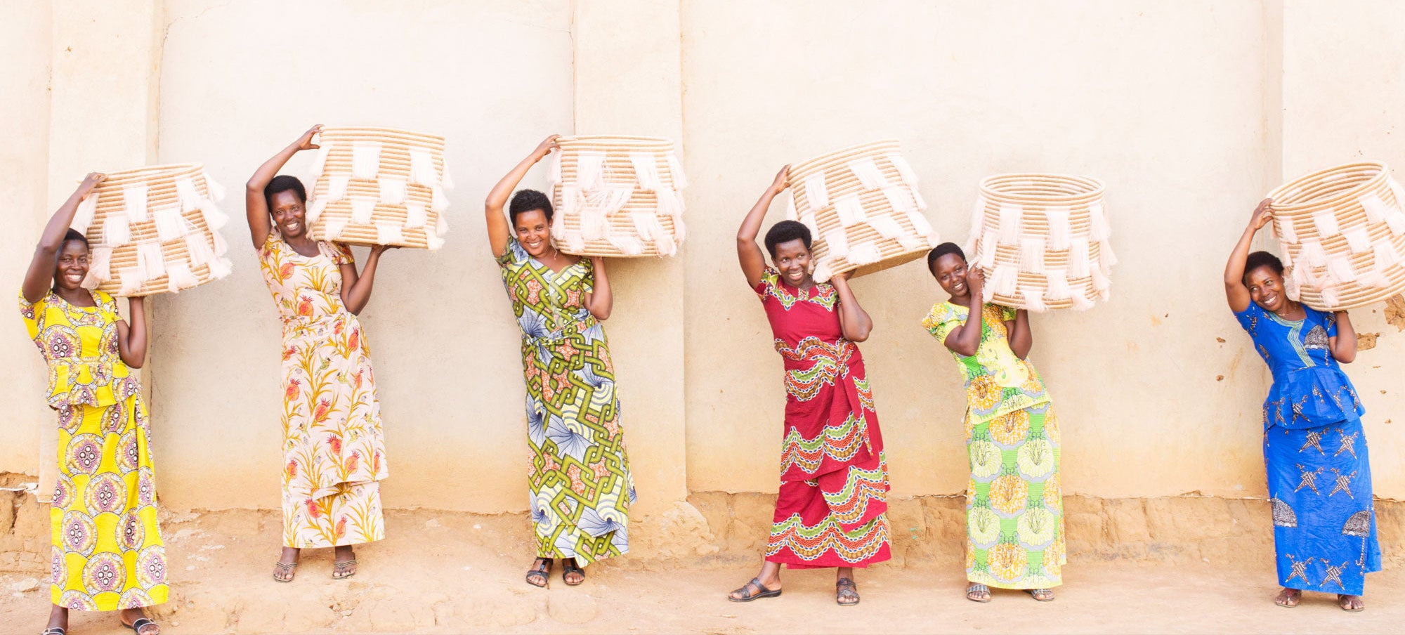 Six women in colorful dresses holding patterned boxes against a light background