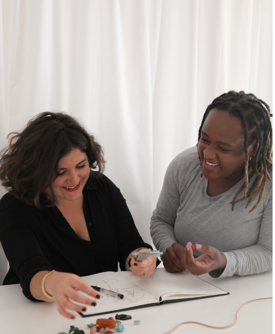 Two women sitting at a table with a white curtain in the background
